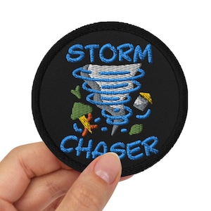 May include: A black embroidered patch with a blue tornado design and the text "STORM CHASER" in blue.
