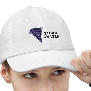 Könnte beinhalten: Weiße Baseballkappe mit einem gestickten Tornado-Design in Schwarz und Lila und dem Text "STORM CHASER".