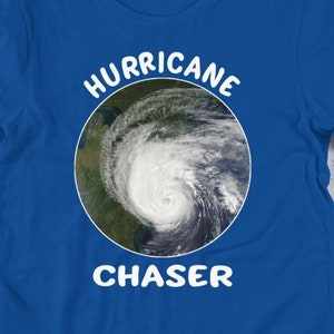 Könnte beinhalten: Ein königsblaues T-Shirt mit einem weißen Kreis-Motiv, das ein Satellitenbild eines Hurrikans zeigt. Der Text "HURRICANE CHASER" ist in Weiß über und unter dem Motiv aufgedruckt.