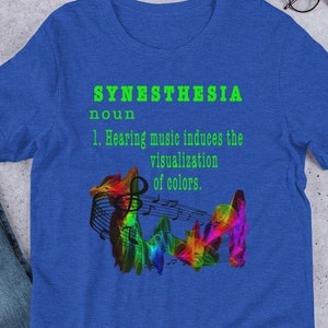 May include: A blue t-shirt with the word "Synesthesia" defined as "Hearing music induces the visualization of colors." The definition is in green text and the word "Synesthesia" is in a green and white font. The shirt features a colorful graphic of musical notes.