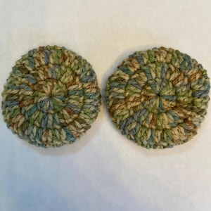 May include: Two crocheted round coasters in shades of green, brown, and blue. The coasters have a circular pattern.