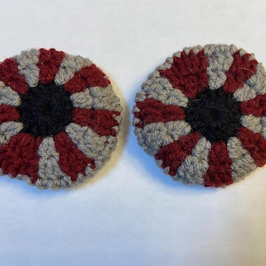 May include: Two crocheted eye-shaped ornaments with a red and gray striped pattern and a black center.