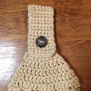 Può includere: Un copribicchiere in crochet beige con un bottone marrone.