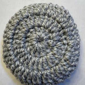 May include: A round, crocheted item in shades of gray and white. The handmade piece features a textured surface created by the looped yarn stitches. The item appears to be a coaster or a similar household accessory.