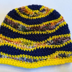 Pode incluir: Um gorro de crochê azul e amarelo com um padrão listrado. O gorro é feito com uma variedade de fios coloridos.