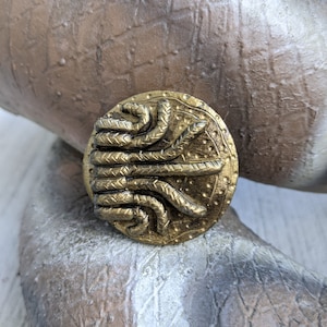 Puede incluir: Un anillo de metal de color dorado con un diseño detallado de serpientes entrelazadas. El anillo es de forma ovalada y tiene una superficie texturizada.