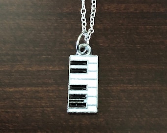 May include: A silver chain necklace with a small silver charm in the shape of a piano keyboard. The charm is black and white.