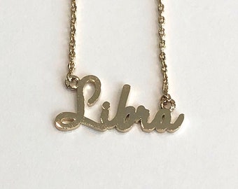 May include: Gold necklace with a cursive 'Libra' pendant.