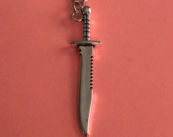 May include: A silver necklace with a silver knife pendant. The knife has a serrated edge and a pointed tip.