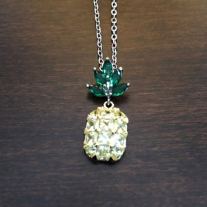 May include: A silver chain necklace with a pineapple pendant. The pineapple is made of yellow and green rhinestones.