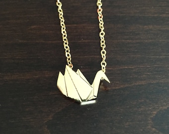 May include: A gold chain necklace with a gold origami swan pendant.