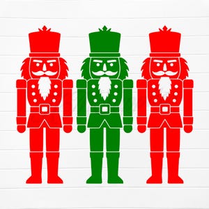 Könnte beinhalten: Drei stilisierte Nussknacker-Figuren in Rot und Grün. Jede Figur hat einen Hut, einen Schnurrbart und einen Bart. Die Figuren tragen eine Uniform mit Gürtel und Stiefeln. Der Hintergrund ist eine weiße Holzmaserung.