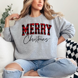 May include: A gray sweatshirt with the words "MERRY" in a red and black plaid design and "Christmas" in a black script font. The sweatshirt is a crew neck style.