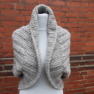 Peut inclure: Un châle gris en tricot avec un col roulé et une coupe ample. Le châle est fait d'un fil doux et texturé et a un design simple et élégant.