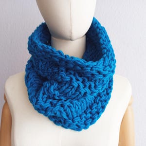 Könnte beinhalten: Ein leuchtend blauer Strickschal, präsentiert auf einer Schaufensterpuppe. Die grobe Strickstruktur ist deutlich sichtbar und erzeugt einen warmen und gemütlichen Eindruck. Der Schal ist einfarbig und für kaltes Wetter geeignet. Der Schal wird um den Hals getragen.