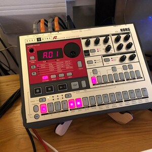 May include: A gray Korg Electribe ER-1 Rhythm Synthesizer with red and white buttons. The display shows "A.D.1".
