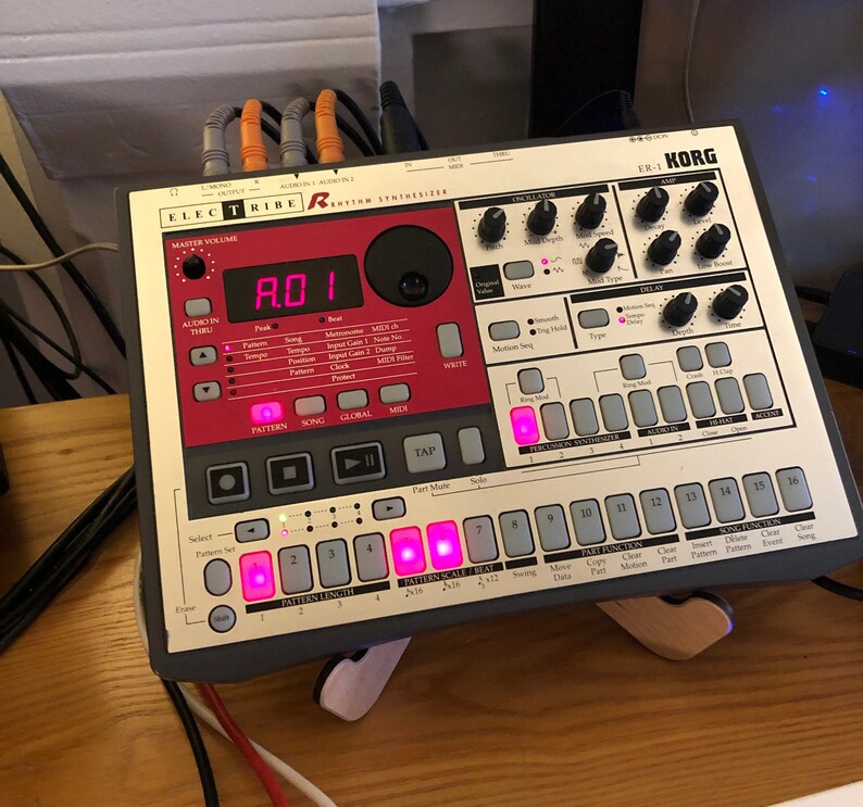 May include: A gray Korg Electribe ER-1 Rhythm Synthesizer with red and white buttons. The display shows "A.D.1".