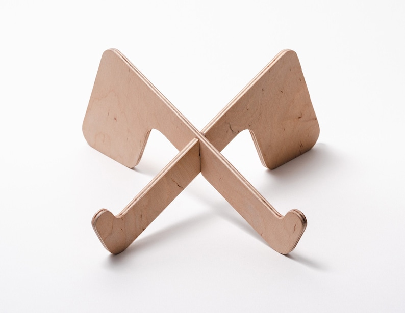 May include: A wooden laptop stand with a simple, minimalist design. The stand is made of light brown wood and has a cross-shaped base.