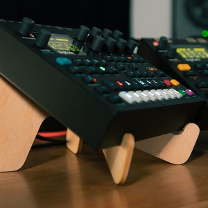 May include: Two black electronic music synthesizers with colorful buttons and knobs, sitting on wooden stands. The synthesizers are on a wooden table.