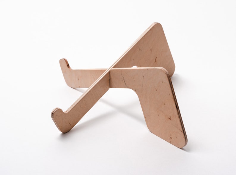 May include: A wooden laptop stand with a natural finish. The stand is made of two pieces of wood that are crossed at the center. The stand is designed to elevate a laptop to a more ergonomic viewing height.