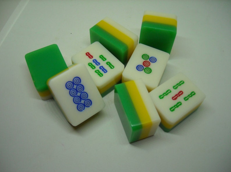 May include: A set of eight green, yellow, and white mahjong tiles with various symbols and numbers. The tiles are arranged in a pile on a white surface.