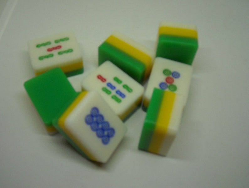May include: A set of nine green, yellow, and white mahjong tiles with various symbols and numbers. The tiles are made of plastic and have a smooth, glossy finish.