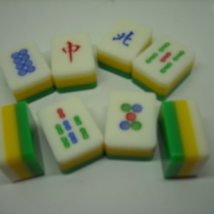 May include: A set of nine colorful mahjong tiles with various Chinese characters and symbols. The tiles are made of plastic and have a white background with green, yellow, and red accents.