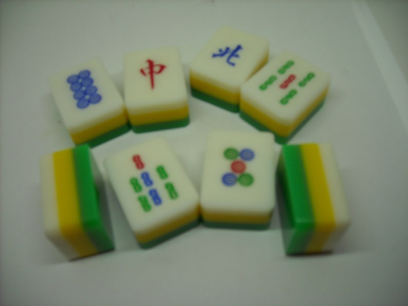 May include: A set of nine colorful mahjong tiles with various Chinese characters and symbols. The tiles are made of plastic and have a white background with green, yellow, and red accents.