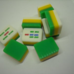 May include: A set of six green, white, and yellow mahjong tiles. The tiles have different symbols and numbers on them.