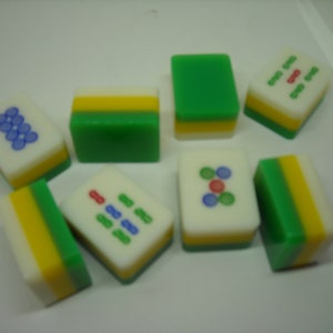 May include: A set of nine green, yellow, and white mahjong tiles with various symbols and numbers. The tiles are arranged in a random pattern on a white surface.