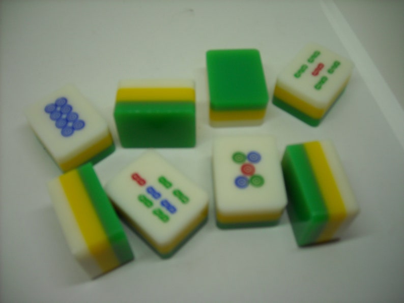 May include: A set of nine green, yellow, and white mahjong tiles with various symbols and numbers. The tiles are arranged in a random pattern on a white surface.