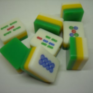 May include: A set of nine green, yellow, and white mahjong tiles with various symbols and numbers. The tiles are arranged in a random pattern on a white surface.