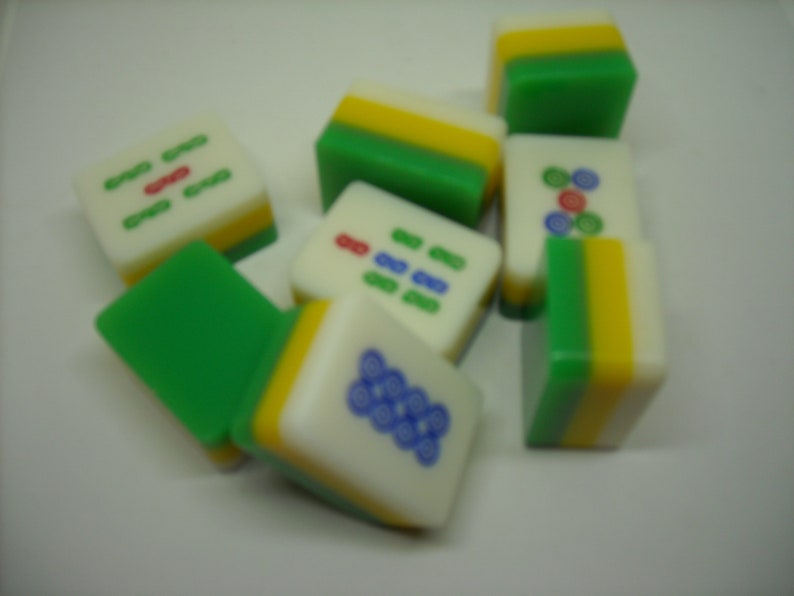 May include: A set of nine green, yellow, and white mahjong tiles with various symbols and numbers. The tiles are arranged in a random pattern on a white surface.