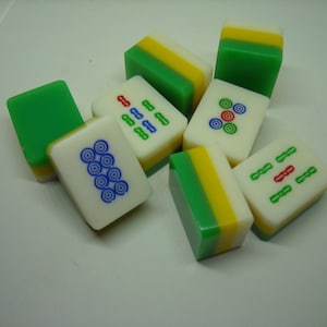 May include: A set of nine green, yellow, and white mahjong tiles with various symbols and numbers. The tiles are arranged in a random pattern on a white surface.