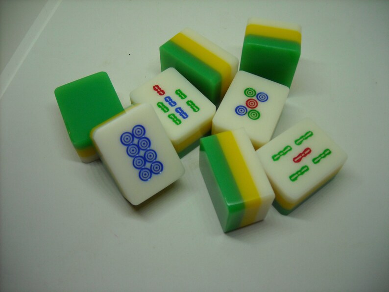 May include: A set of nine green, yellow, and white mahjong tiles with various symbols and numbers. The tiles are arranged in a random pattern on a white surface.