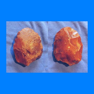 Peut inclure: Deux pierres bruns-rouges, grossièrement taillées, sont présentées sur un fond bleu. Les pierres ont des formes irrégulières et des surfaces texturées, suggérant des artefacts naturels, peut-être anciens.