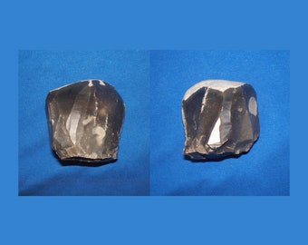 May include: Two dark gray flint stones with a white streak running through them. The stones are on a blue background.