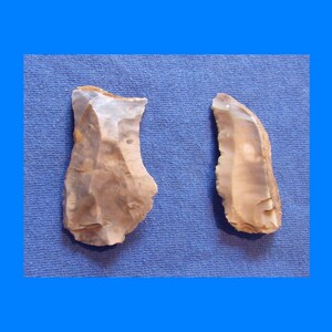 May include: Two flint tools with rough edges and a light brown and gray color. The tools are likely hand-chipped and appear to be ancient artifacts. They are set against a blue background.