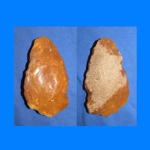 May include: Two views of a roughly shaped, orange-brown stone tool, possibly a hand axe or scraper. One side is smooth and polished, while the other has a lighter, textured coating. The background is a blue fabric.
