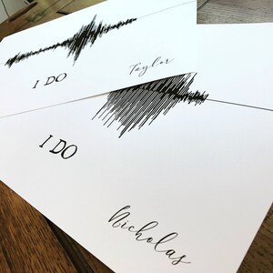 May include: Two white cards with black ink. The top card has a sound wave graphic and the text "I DO" and "Taylor". The bottom card has a sound wave graphic and the text "I DO" and "Nicholas".