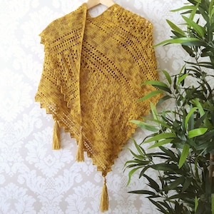 May include: A crocheted shawl in a mustard yellow color with a delicate lace pattern and fringe tassels.