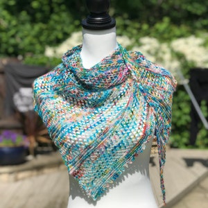 May include: A white, blue and multi-coloured crocheted shawl with a lacy pattern. The shawl is draped over a white mannequin.