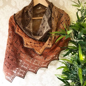 May include: A crocheted shawl in shades of brown, orange, and beige. The shawl has a delicate lace pattern and a scalloped edge.