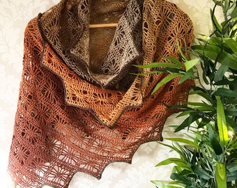 May include: A crocheted shawl in shades of brown, orange, and beige. The shawl has a delicate lace pattern and a scalloped edge.