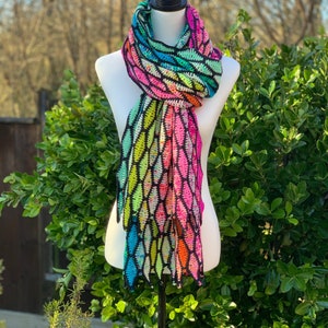 May include: A colorful crocheted scarf with a black background and a geometric pattern. The scarf is made with a variety of bright colors, including pink, green, blue, and yellow.