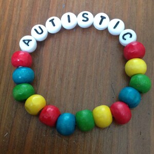 Peut inclure: Un bracelet en perles de bois color&eacute;es avec le mot "AUTISTIC" &eacute;crit en perles blanches.