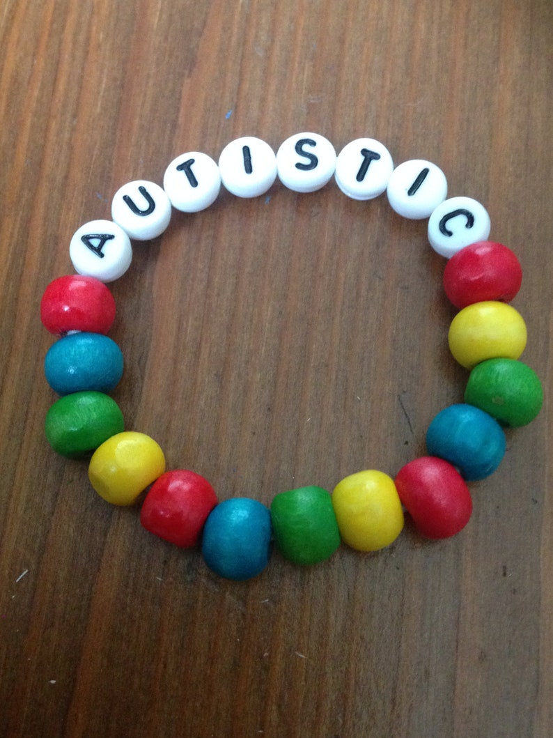 Peut inclure: Un bracelet en perles de bois color&eacute;es avec le mot "AUTISTIC" &eacute;crit en perles blanches.