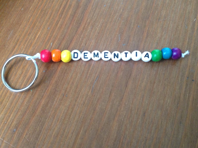 Peut inclure: Un porte-cl&eacute;s en perles color&eacute;es avec le mot "DEMENTIA" &eacute;crit en perles blanches avec des lettres noires.