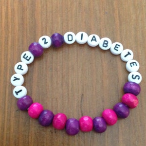 Peut inclure: Un bracelet en perles violettes et roses avec les mots "TYPE 2 DIABETES" &eacute;crits en lettres blanches.