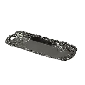 May include: A rectangular, dark gray serving tray with a decorative grape and leaf design on the ends and edges. The tray is made of metal and has a smooth, reflective surface. The tray is approximately 15 inches long.